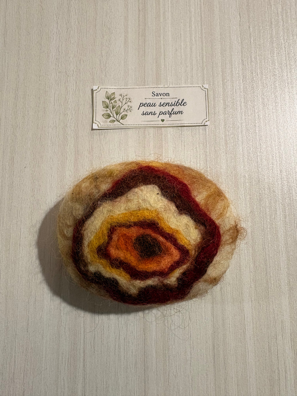 Savon feutré artisanal Terre d’automne pour peau sensible, sans parfum, en laine naturelle aux teintes orange, bordeaux et crème.